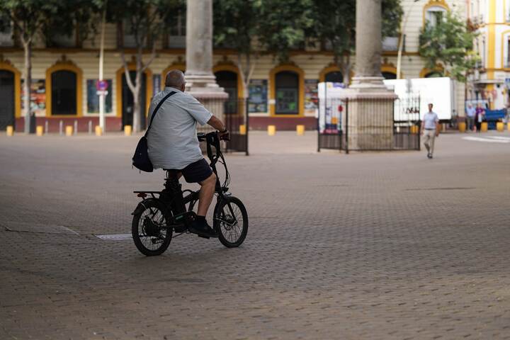 小さな肩掛けバッグを身につけて広場を自転車で走る男性
