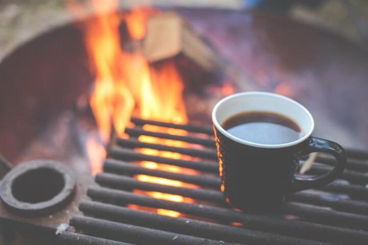 焚き火のそばの焼き網に置かれた黒いコーヒーマグ